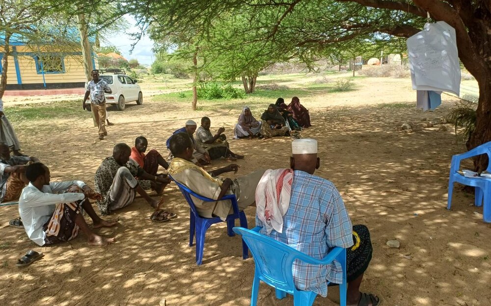 Community assembly gathered under a tree for a joint planning session